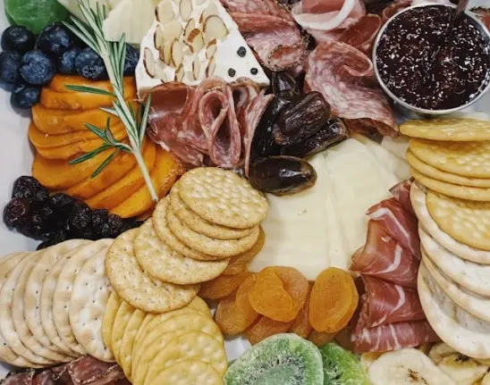 Foto de cima de uma mesa posta de coffee break para empresas com queijos, frios e bolachas