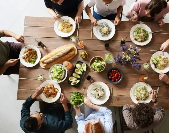 foto de cima de um grupo de oito colegas de trabalho em torno de uma mesa retangular, almoçando aquilo que parecem ser pratos feitos