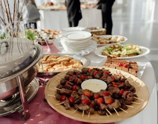 Uma mesa de comida árabe com um prato de kafta em destaque e outras opções de salada fria de uma coziha terceirizada