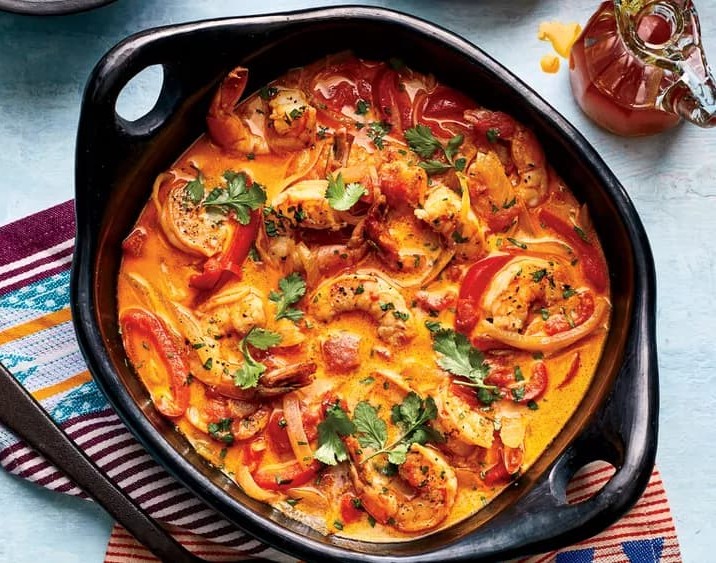Foto vista de cima de uma cumbuca de moqueca gratinada servida sobre uma mesa branca, feita com alguns ingredientes vindos de fora do Brasil em uma clara mostra da tendência gastronômica para 2025